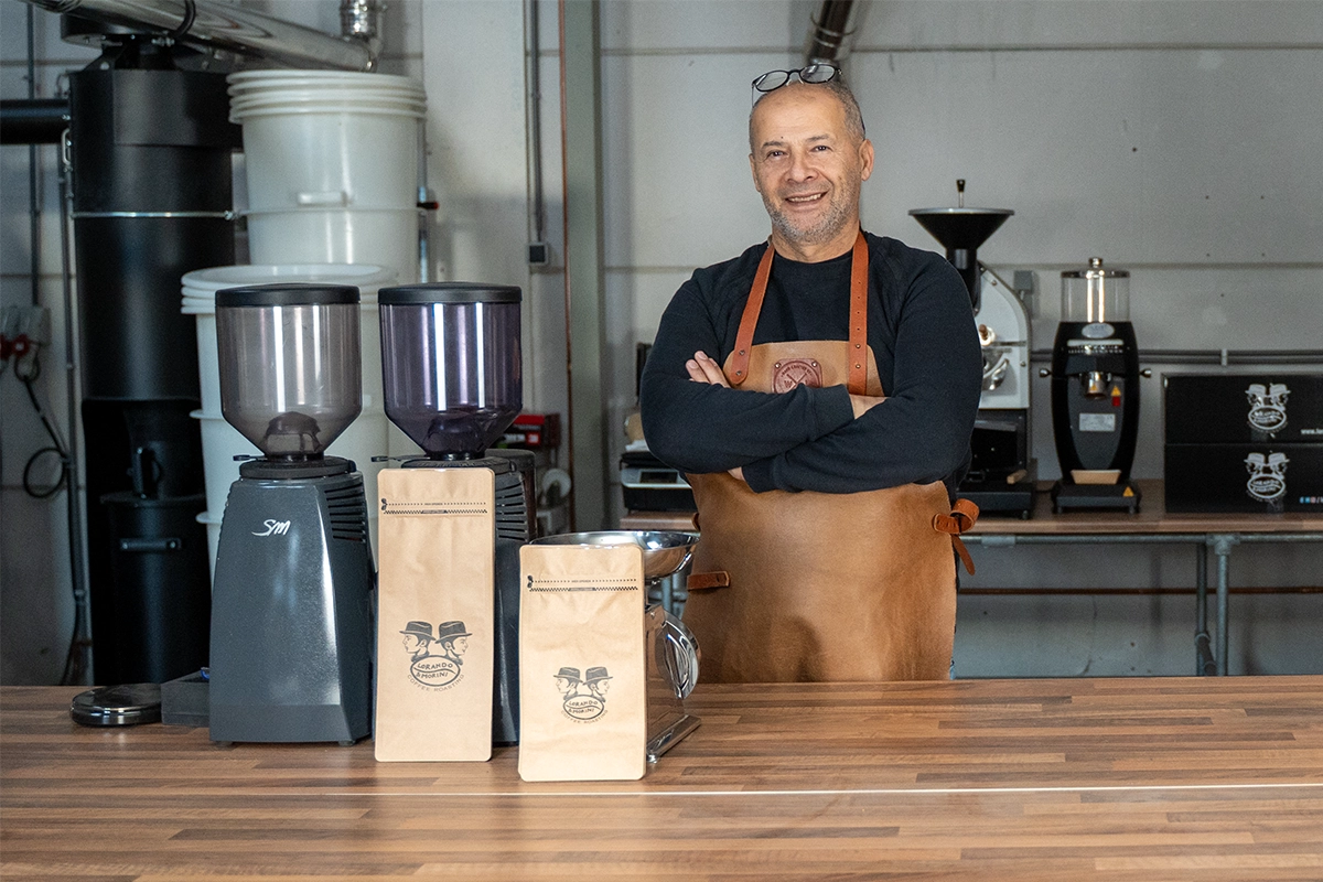 Dos van Lorando & Morini staat in zijn koffiebranderij naast koffiemolens en verpakkingen met specialty koffiebonen.