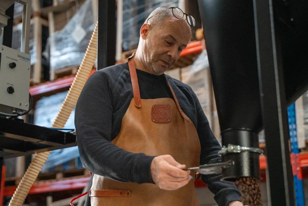 Dos van Lorando & Morini schept vers gebrande koffiebonen uit de koffiebrander in de branderij.