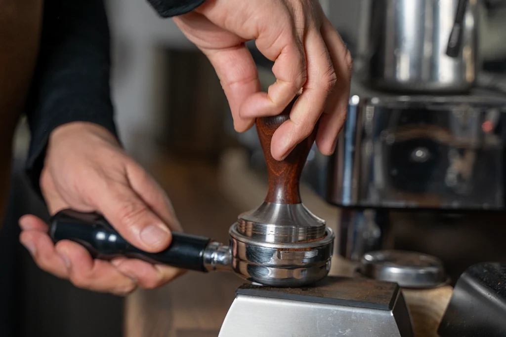 Barista die gemalen koffie aandrukt met een tamper in een portafilter voor het zetten van espresso.