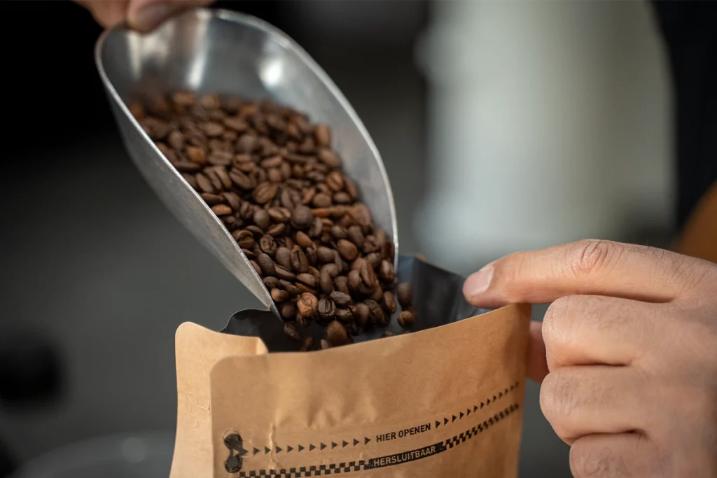 Vers gebrande koffiebonen die met een schep in een Lorando & Morini koffieverpakking worden gegoten.